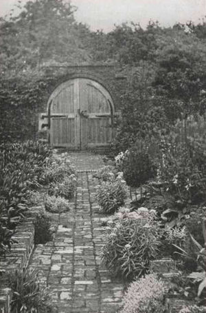 Toegang tot de poort langs een klinkerpaadje met bloemen aan weerszijden